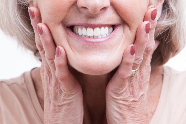 A woman with dentures smiling with her hands up to her face.