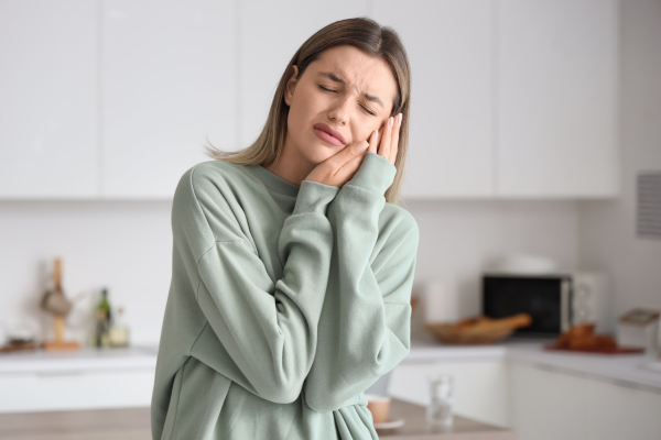 A woman experiencing dental pain while standing in her kitchen.