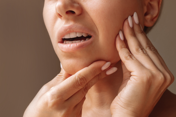A woman holding her jaw due to pain from TMJ disorder.