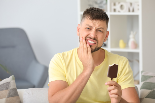A man holding an icea cream bar with his hand up to his face due to tooth sensitivity.