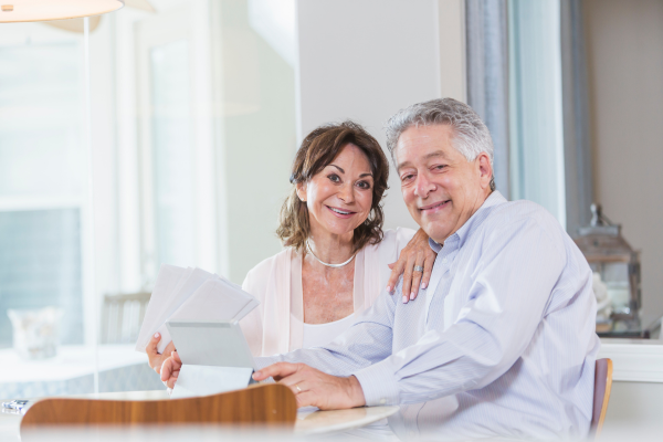A senior woman and man sitting at a desk holding envelopes.
